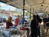 A group of six people stand in front of a table at a festival while the vendor speaks to them