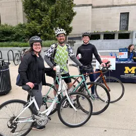 Bike to Wherever Day event participants are featured with their bikes, a man, woman and male teen, alongside a University of Michigan information table