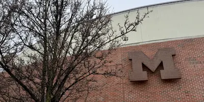 Closeup of brick exterior of University of Michigan Crisler Arena with the university's Block M logo on the wall and a tree in the foreground