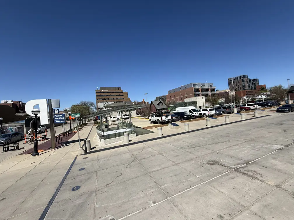 Parking lot site of Library Lane in Ann Arbor with cars parked and blue sky with buildings in the background