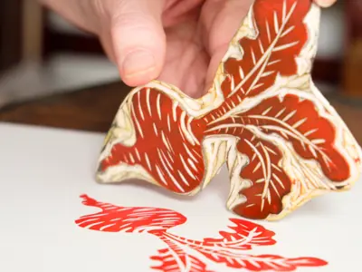A person uses a stamp in the shape of a beet to print on a piece of paper