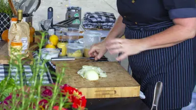 Cutting board and hands surrounded by vegetables and kitchen items
