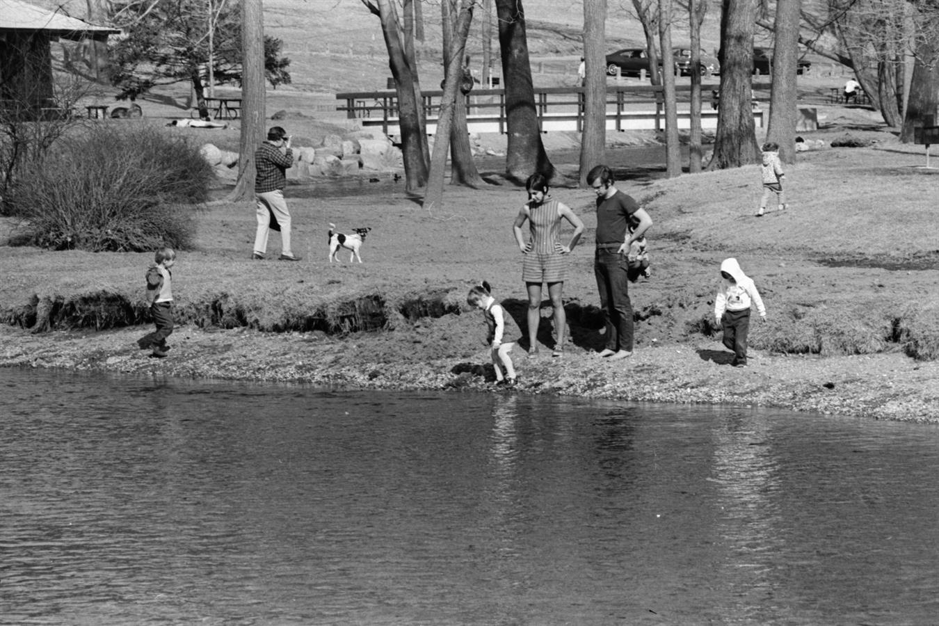 Black and white photo of people standing that the water's edge in Island Park